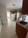 Kitchen with stove, freestanding refrigerator, brown cabinetry, light stone counters, and light tile patterned floors
