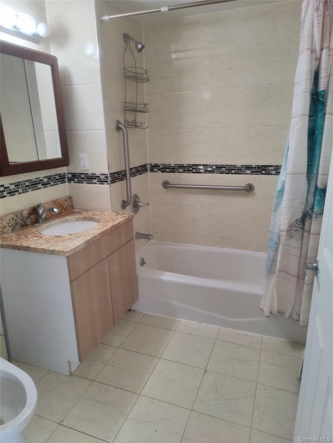 Bathroom featuring shower / bath combination with curtain, vanity, a bidet, tile walls, and light tile patterned floors