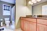 Hall Bathroom featuring a wood-finish vanity with a dark granite countertop and integrated sink, a large wall-mounted mirror, and a sconce light fixtu