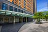 Building entrance featuring a glass canopy, large format stone-finish tile, stone-clad facade, and a modern brick-and-glass tower
