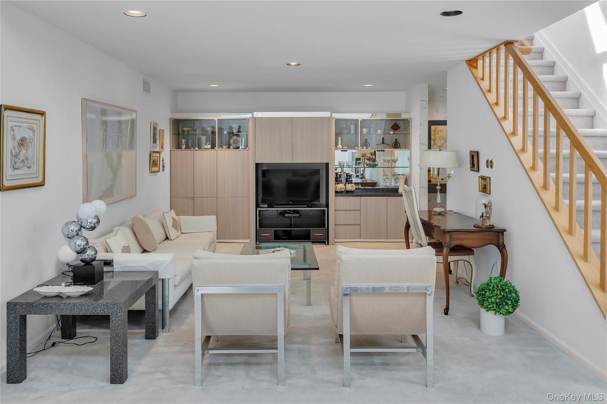 Recessed lighting illuminates this living space featuring light wood-finish built-in cabinetry, a built-in bar area with a mirrored backsplash, and a