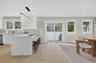 Expansive kitchen island with waterfall countertop, white shaker cabinetry, stainless steel appliances, and wood-finish flooring
