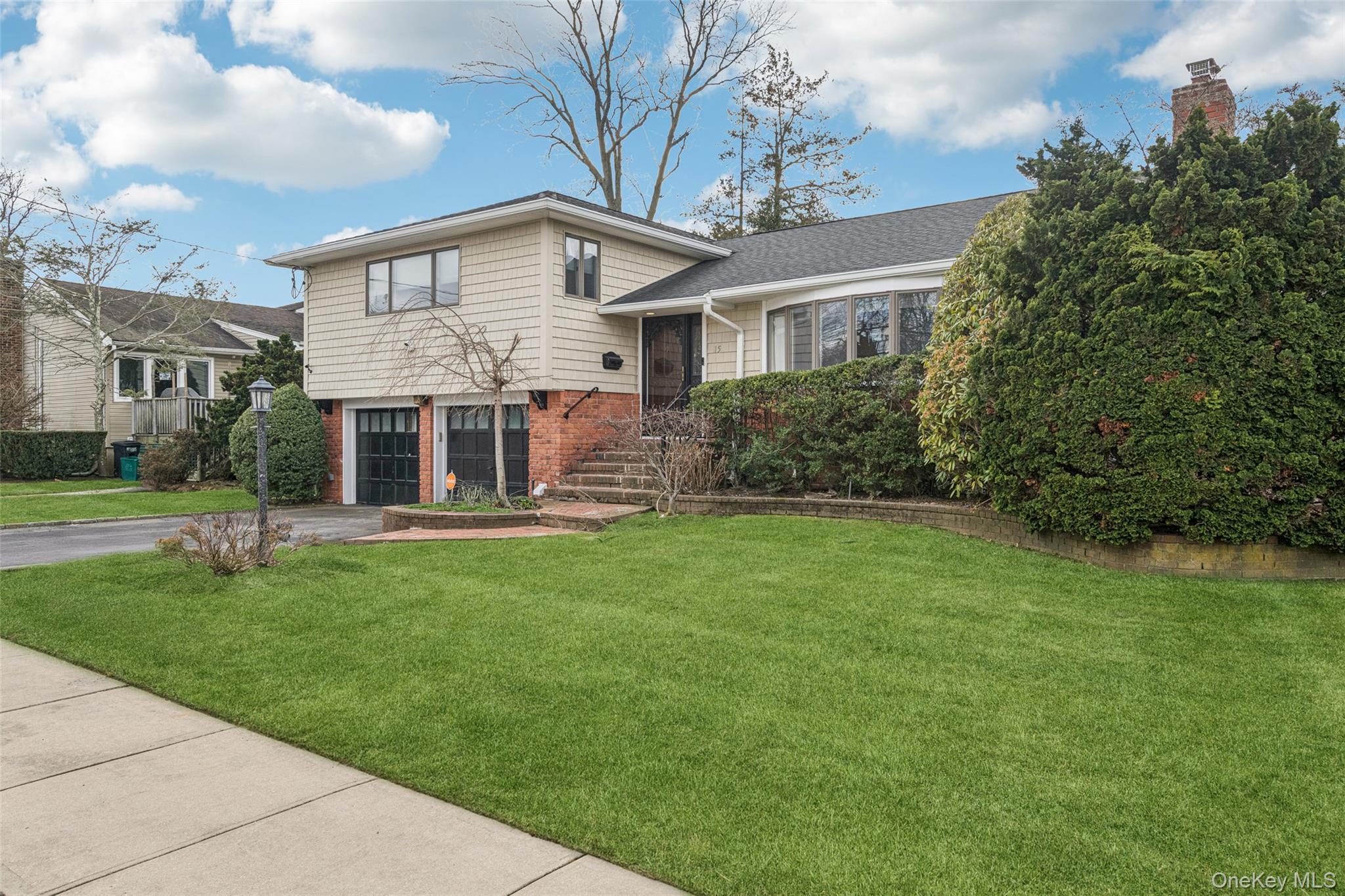 Tri-level home with brick siding, driveway, a front yard, and an attached garage