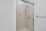 Primary shower with new chrome fixtures, and a handheld shower head, and new glass doors