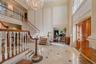 Grand entry foyer featuring a sweeping staircase with detailed balusters and wood handrails, marble flooring with accent inlays, and a multi-tiered cr