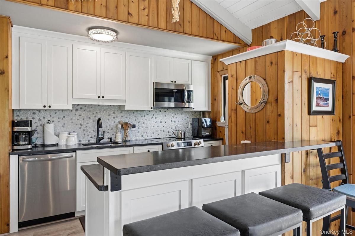 Kitchen featuring white shaker-style cabinetry, a gray mosaic tile backsplash, black countertops, and stainless steel appliances