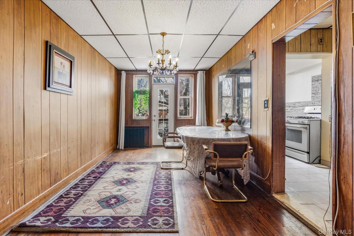 Dining room with a chandelier, wood walls, light wood finished floors, and a drop ceiling