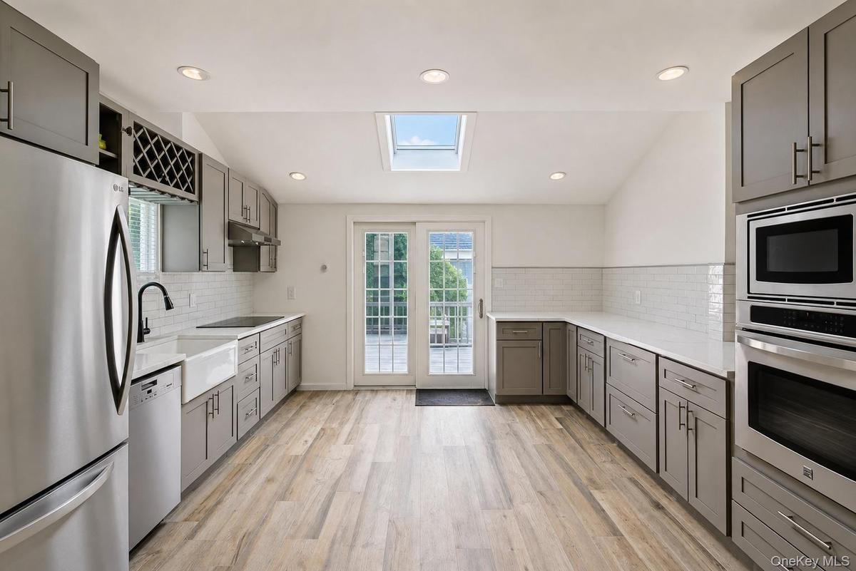 Kitchen featuring wood-finish flooring, gray cabinetry, built-in stainless steel appliances, a white farmhouse sink with a matte black faucet, and a s