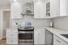 Kitchen with appliances with stainless steel finishes, wall chimney exhaust hood, light stone countertops, and white cabinetry