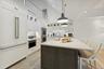 kitchen breakfast bar, white cabinets, an island with sink, light stone counters, and hanging light fixtures