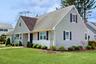 Cape cod home featuring roof with shingles, a chimney, and a front lawn