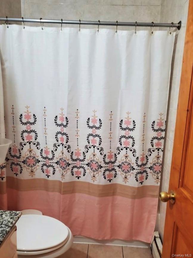 Full bath featuring curtained shower, baseboard heating, vanity, and tile patterned flooring