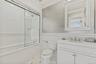 Full bath with vanity, tiled shower / bath, a wainscoted wall, tile walls, and crown molding.