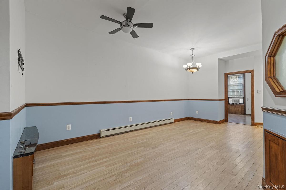 Empty room featuring a baseboard radiator, light wood-type flooring, a chandelier, and a ceiling fan