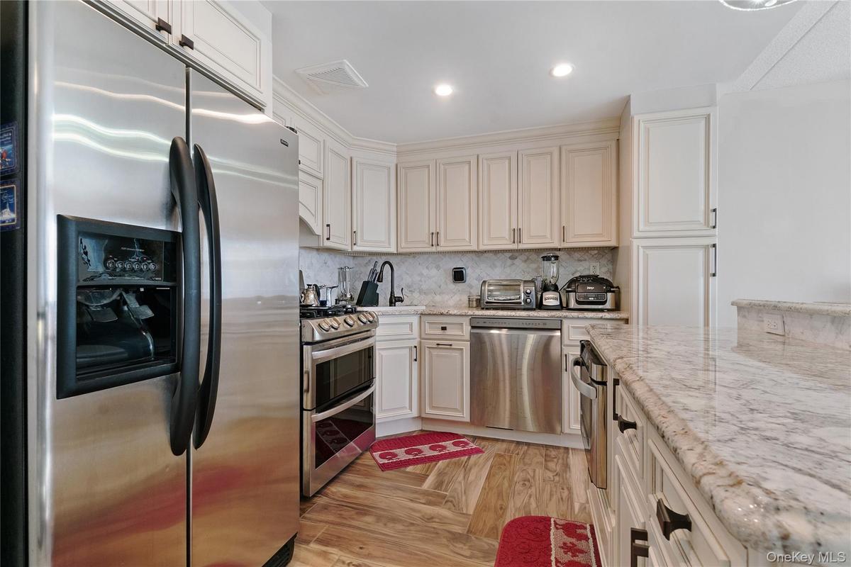 Kitchen featuring wood-finish flooring, stainless steel appliances, light-toned cabinetry with dark hardware, a stone countertop, and a tiled backspla