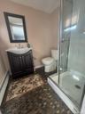 Three-quarter bathroom featuring a stall shower with a clear glass enclosure, a dark wood-finish vanity with a white basin sink, and a framed mirror