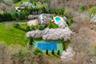 Aerial perspective showcasing a comprehensive property layout with a tennis court, swimming pool, extensive green lawns, mature trees, and a stone-cla