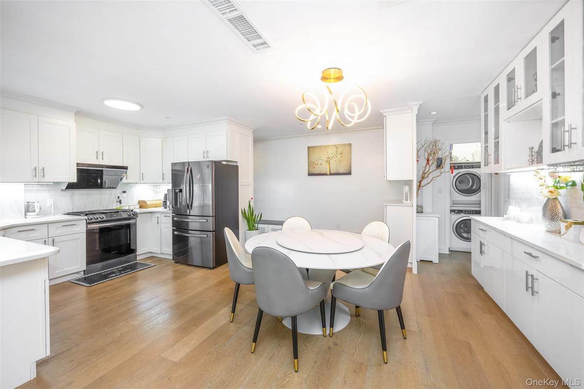 Dining room with stacked washer / dryer, light wood-style floors, ornamental molding, and a chandelier