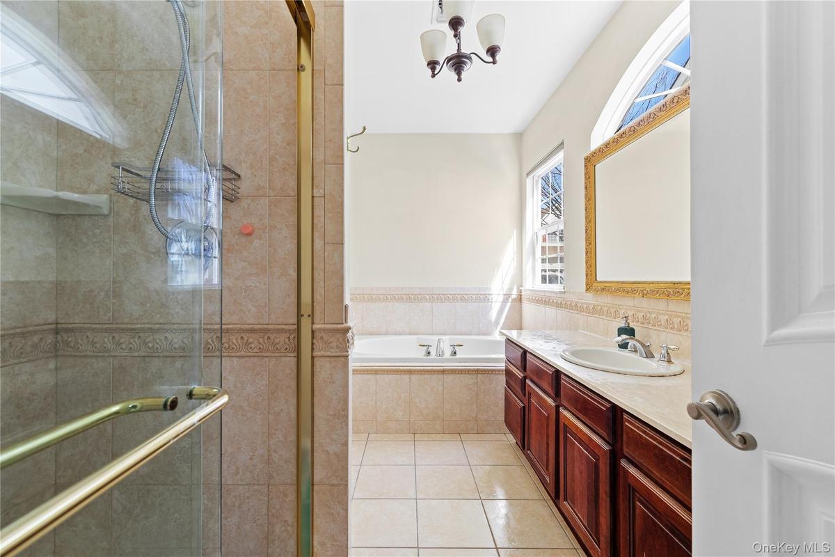 Tiled shower enclosure with a glass door, built-in bathtub, dual windows, and a vanity with an integrated sink and wood-finish cabinetry