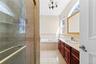 Tiled shower enclosure with a glass door, built-in bathtub, dual windows, and a vanity with an integrated sink and wood-finish cabinetry