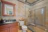 Bathroom featuring a glass-enclosed shower with custom tile work, a wood-finish vanity with a built-in sink, a dark countertop, and a wall-mounted mir