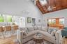 Living area with a ceiling fan, high vaulted ceiling, light wood-type flooring, an AC wall unit, and a skylight