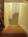 Hardwood staircase with natural wood treads and a dark wood newel post leading to a lower level with wood-finish flooring