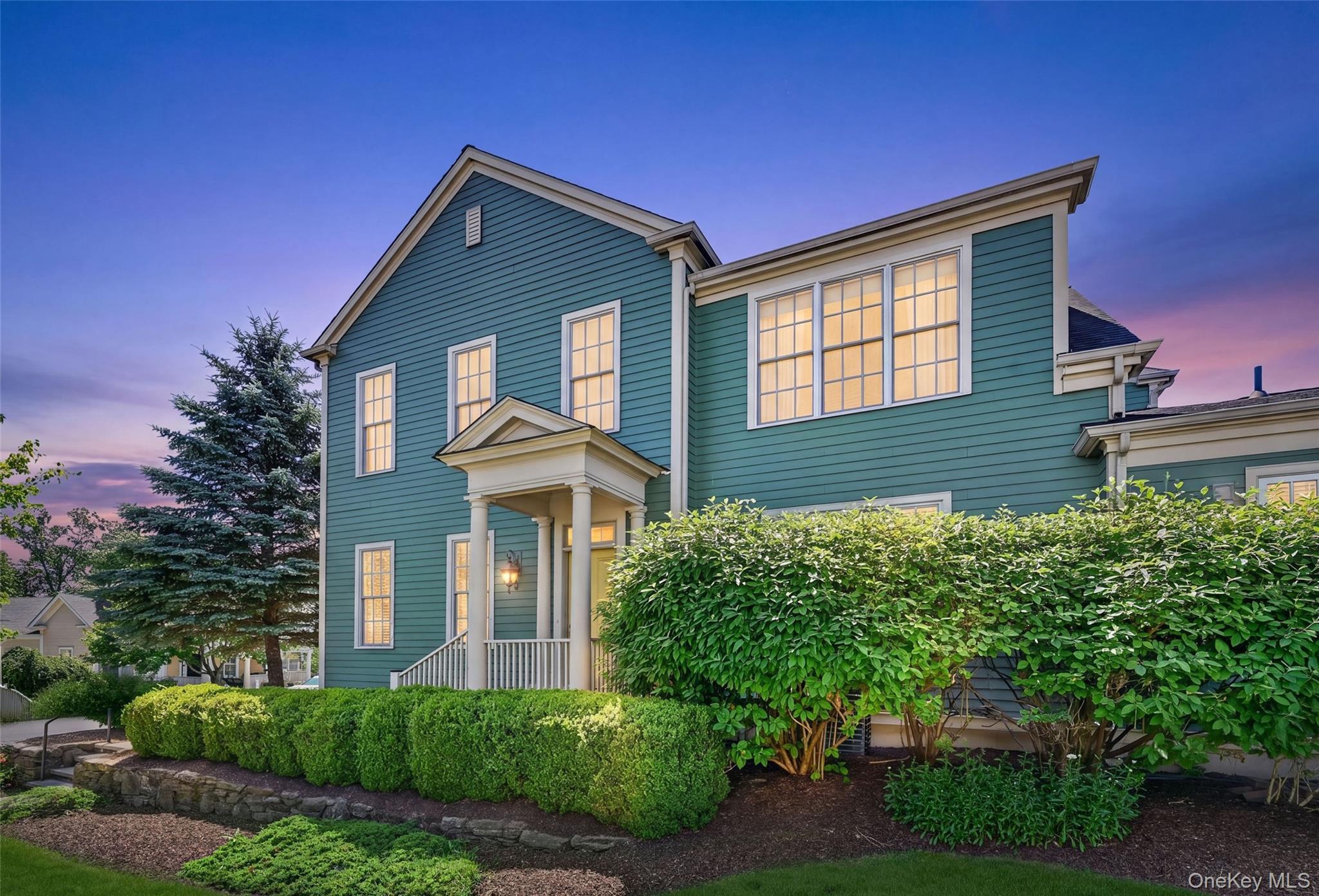A beautiful twilight view highlights the home’s classic architecture, welcoming front entry, glowing windows, and mature landscaping.