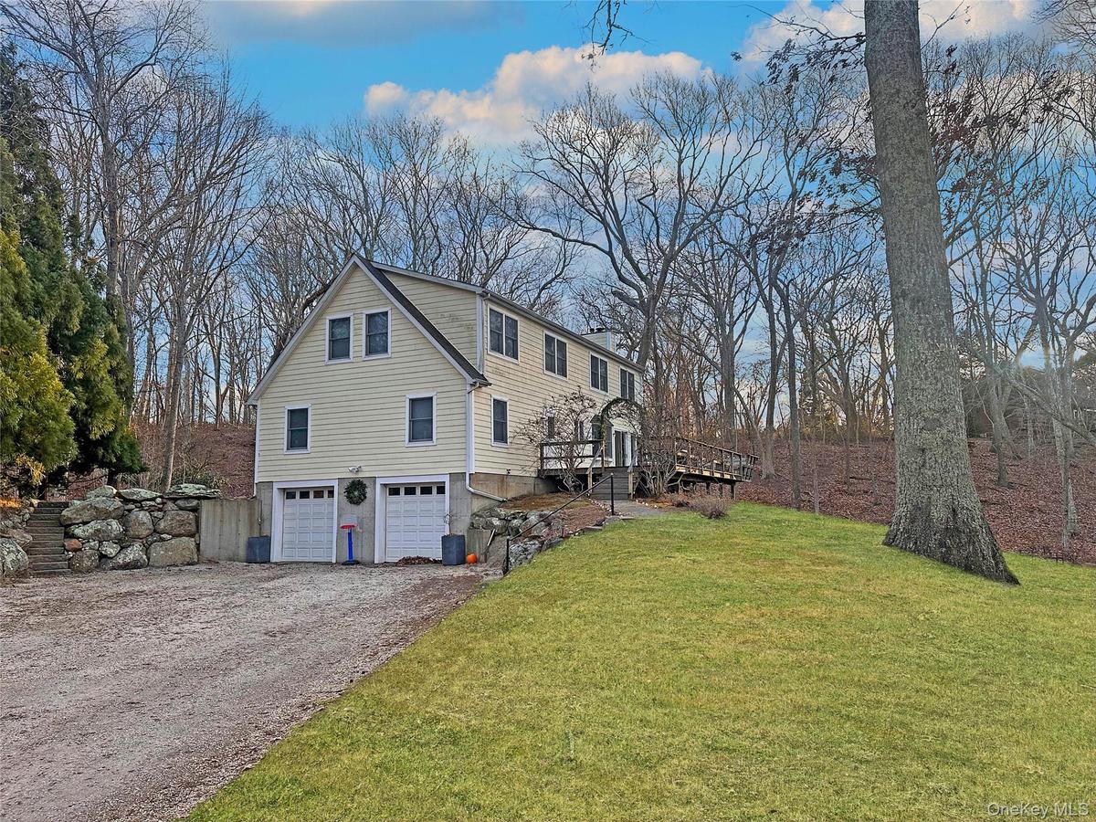 View of property exterior featuring a yard, an attached garage, a wooden deck, driveway, and a chimney