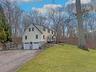 View of property exterior featuring a yard, an attached garage, a wooden deck, driveway, and a chimney