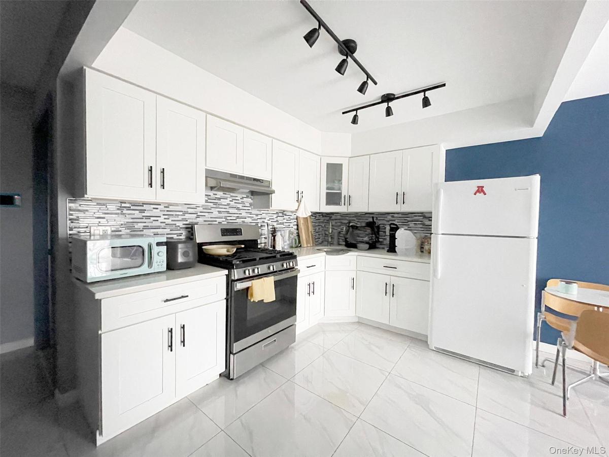Kitchen with white cabinetry, white appliances, tasteful backsplash, and light countertops