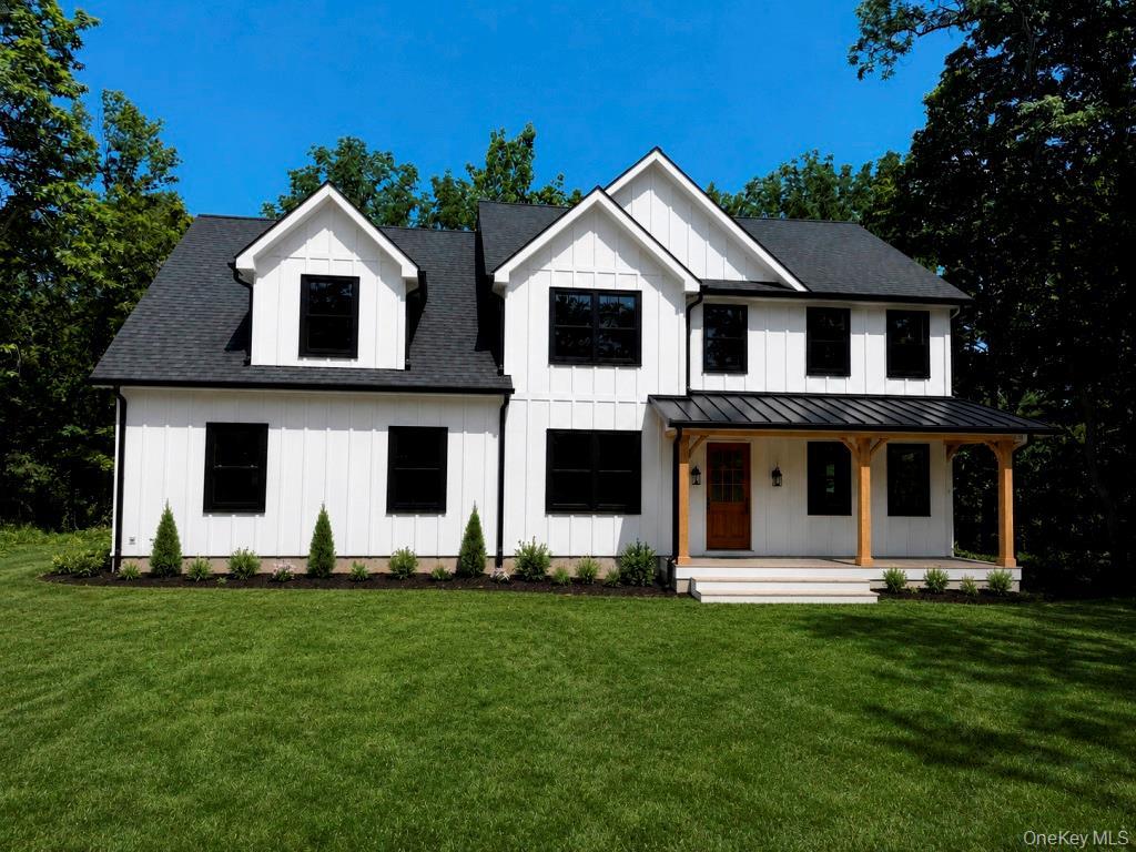 Modern farmhouse exterior featuring board and batten siding, a covered porch with wooden beams, black-framed windows, and a black metal roof accent