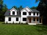 Modern farmhouse exterior featuring board and batten siding, a covered porch with wooden beams, black-framed windows, and a black metal roof accent
