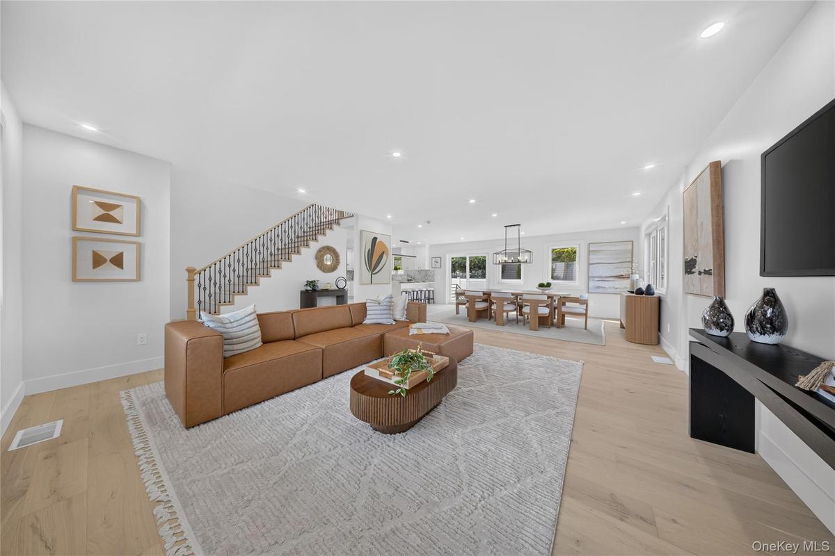 Open-concept interior featuring wood-finish flooring, recessed lighting, a staircase with decorative balusters, and multiple windows