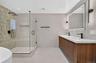Glass-enclosed shower with a tiled wall and integrated niche, dual vanity with wood-finish cabinetry, and an illuminated mirror with modern sconces