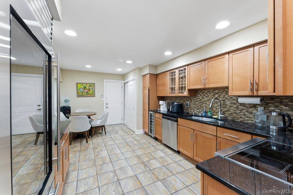 Kitchen featuring wood cabinetry, dark countertops, a mosaic tile backsplash, stainless steel appliances, and tile flooring