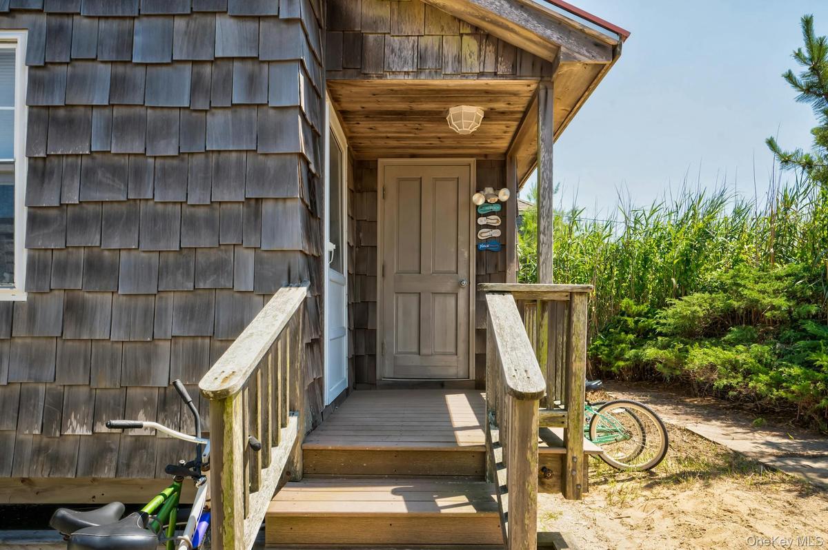 Exterior featuring wood shingle siding, an inviting covered entry porch, a wood-finish door, and natural landscaping with tall grasses