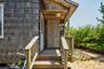 Exterior featuring wood shingle siding, an inviting covered entry porch, a wood-finish door, and natural landscaping with tall grasses