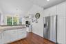 Kitchen featuring white cabinets, stainless steel refrigerator with ice dispenser, lofted ceiling, dark wood-type flooring, and light stone counters