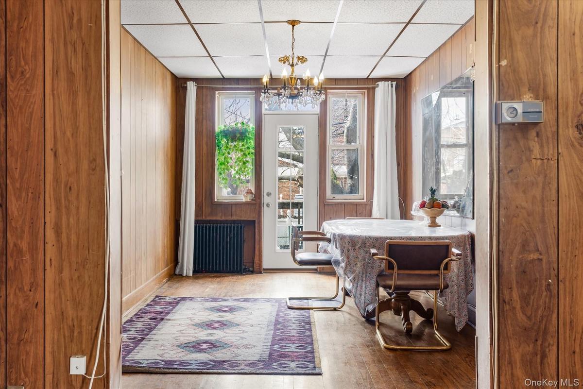 Dining room with radiator heating unit, wooden walls, a chandelier, a paneled ceiling, and wood finished floors