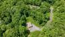Expansive wooded grounds featuring a detached structure, gravel driveway, and a partially visible swimming pool