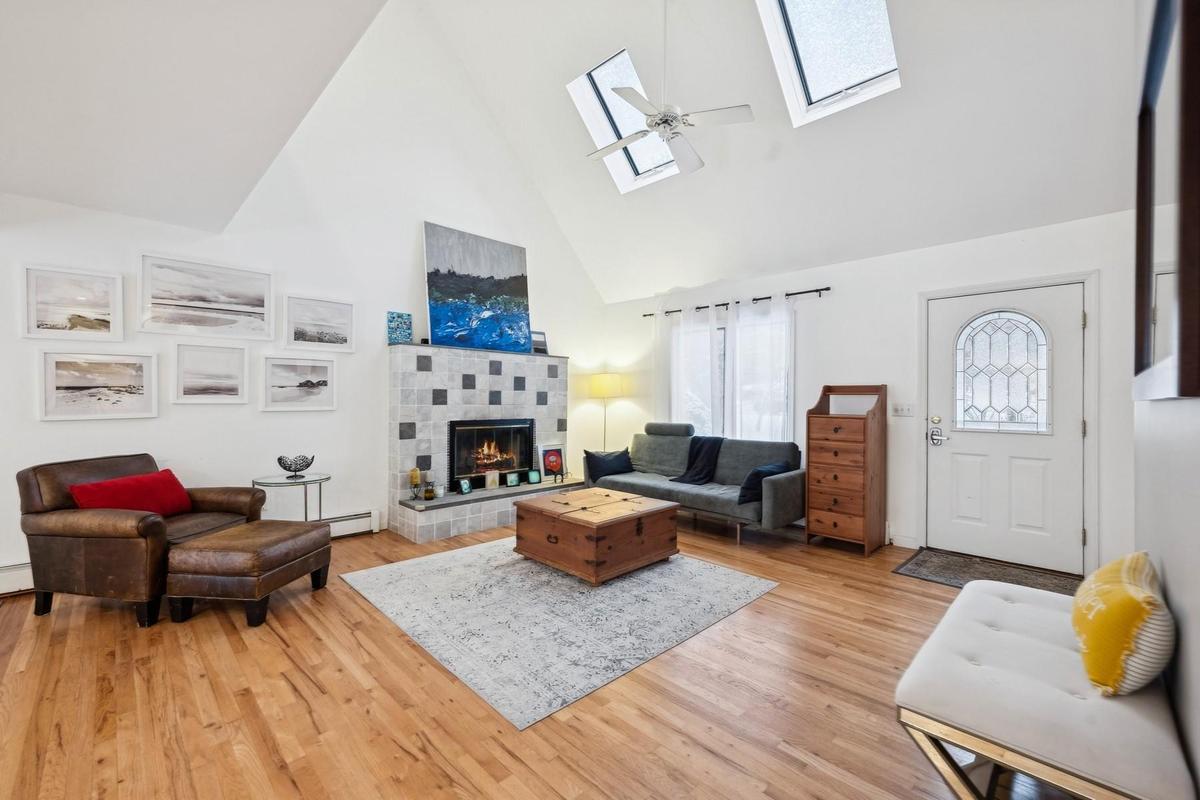 Living room with a healthy amount of sunlight, a tiled fireplace, high vaulted ceiling, and a skylight