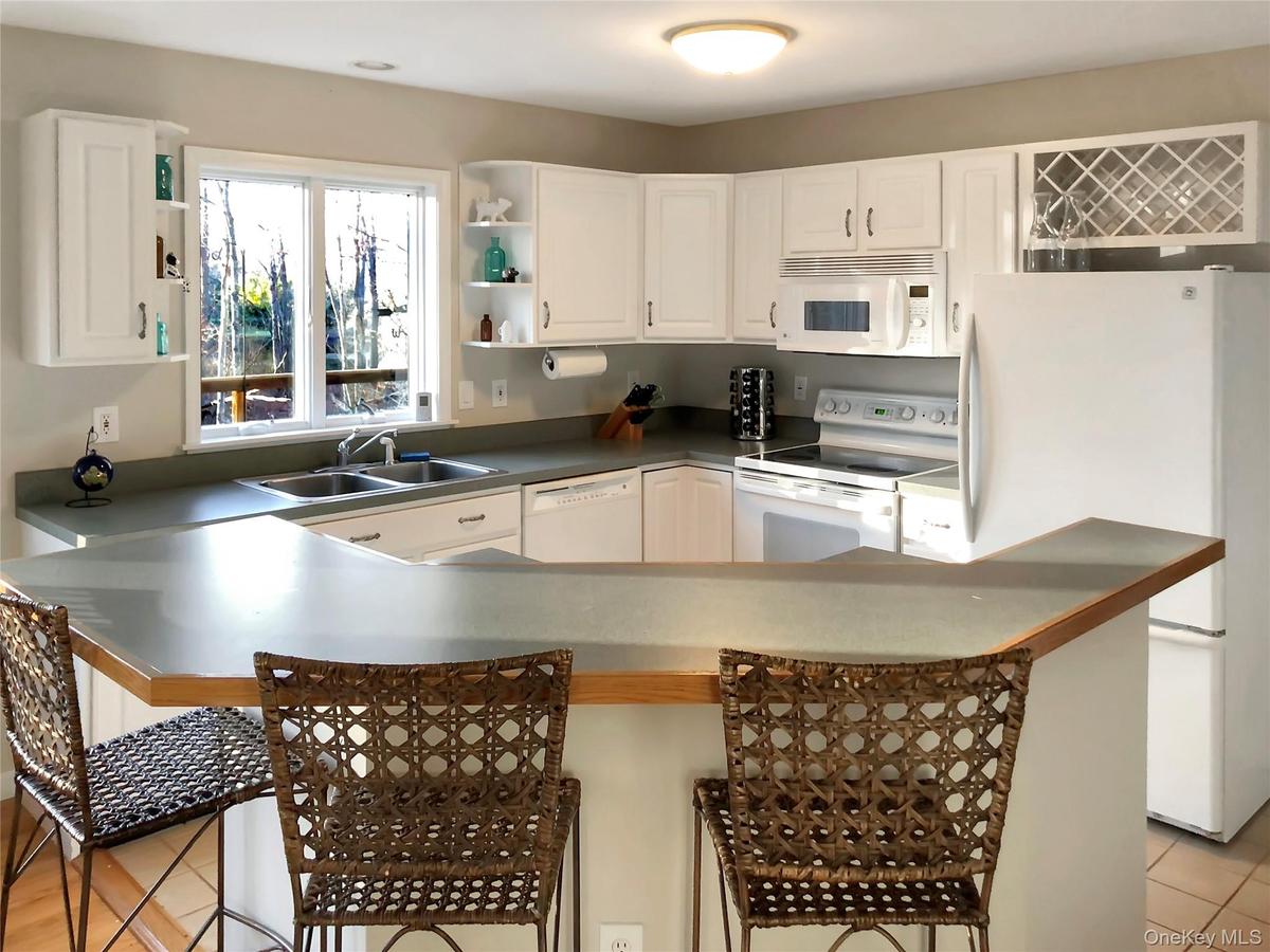 Kitchen featuring white appliances, white cabinetry, a breakfast bar area, open shelves, and dark countertops