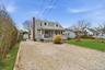 Cape cod house with a porch, a storage shed, a chimney, and gravel driveway