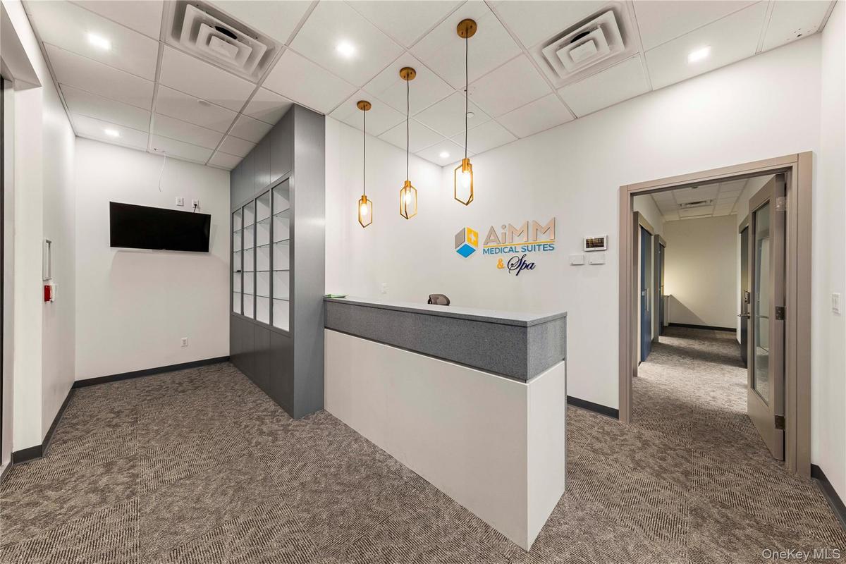 Modern reception area featuring a built-in white and gray reception desk, three gold-toned pendant lights, and textured gray carpeting