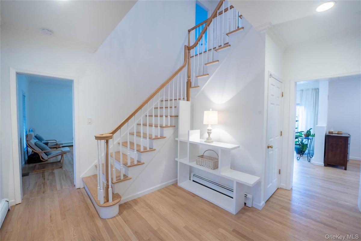 Staircase featuring baseboards, a baseboard heating unit, crown molding, and wood finished floors