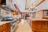 Gourmet kitchen featuring a professional-grade range with a mosaic tile backsplash, custom wood cabinetry, extensive stone countertops, a large center
