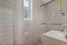 Bathroom featuring extensive wall and floor tiling, a single-pane window, and a vanity with an integrated sink