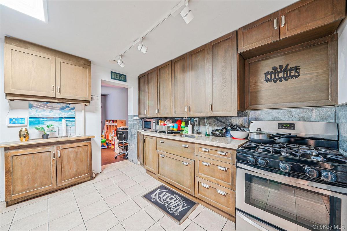 Kitchen featuring stainless steel appliances, rail lighting, light tile patterned flooring, decorative backsplash, and light stone countertops