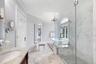Marble-finish flooring, glass-enclosed shower with tile base, freestanding bathtub, and a double-hung arched window